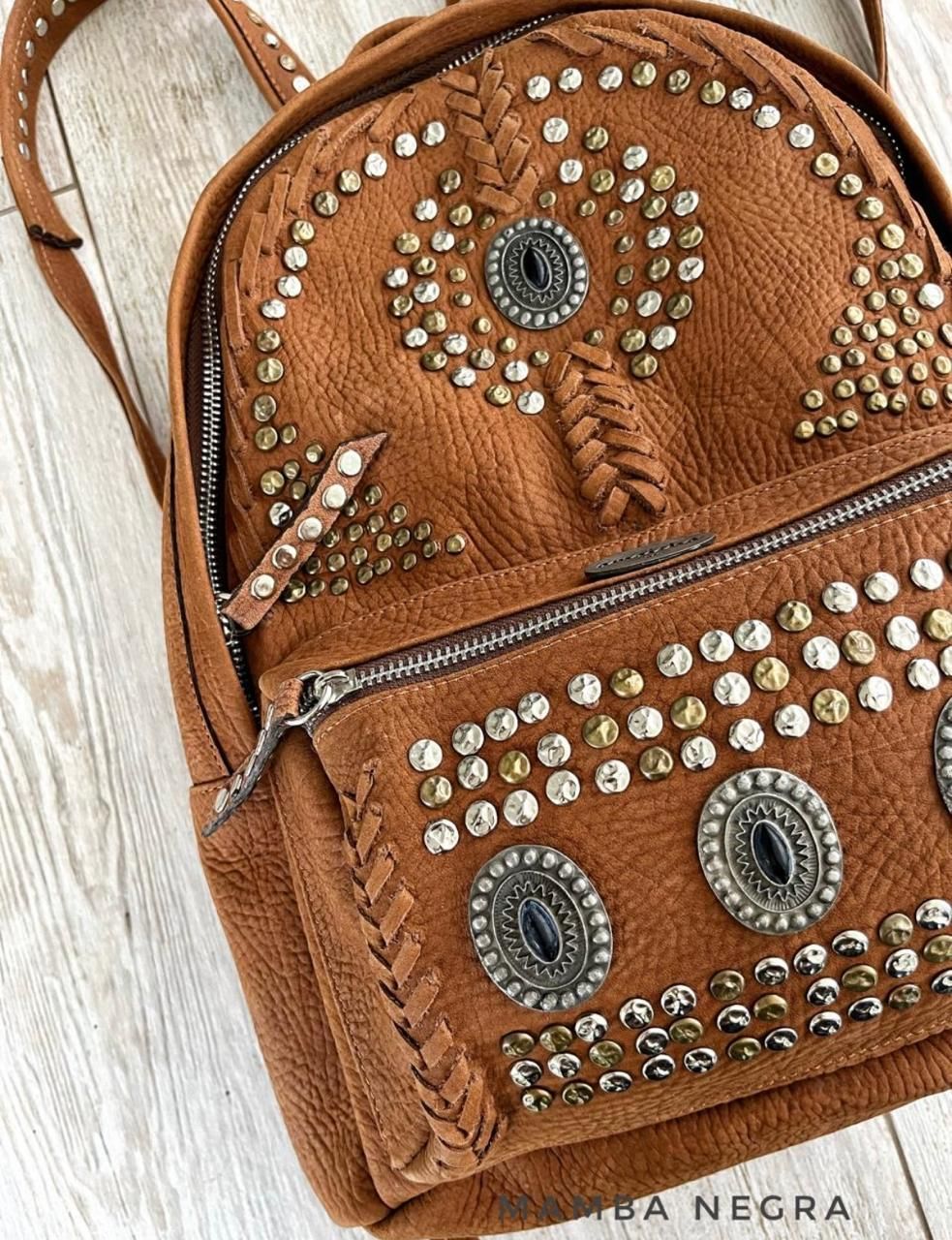 Una mochila de cuero marrón texturizado adornada con tachuelas plateadas y doradas