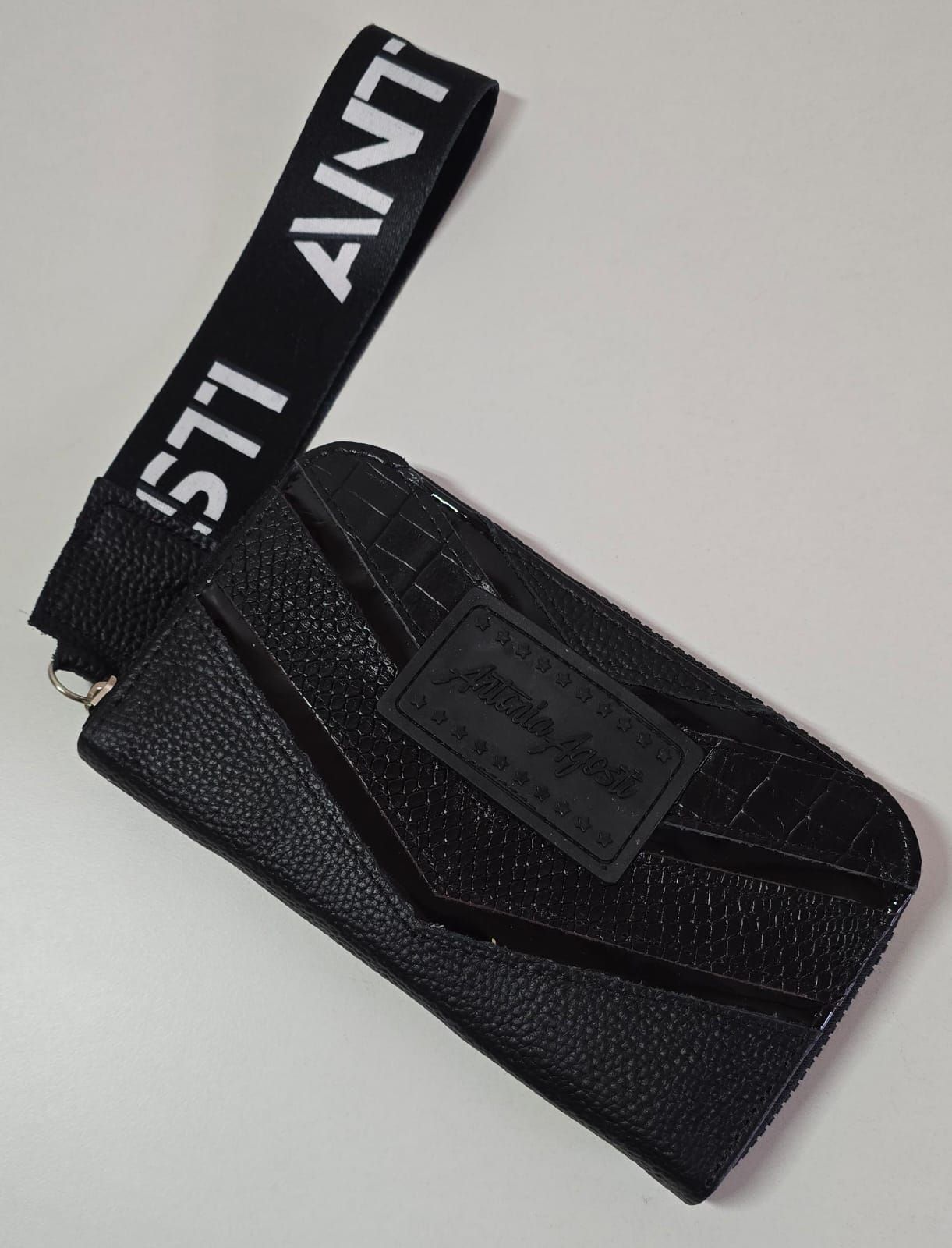 Una billetera de cuero sintético de color negro con acabado texturizado, un bolsillo con costuras en forma de chevron