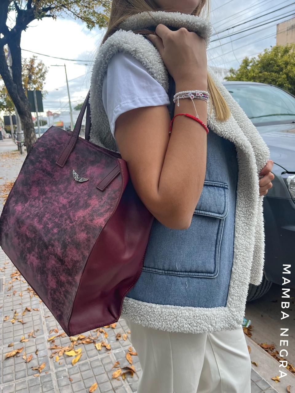 Una persona lleva un bolso oscuro con estampado mientras viste un chaleco de mezclilla