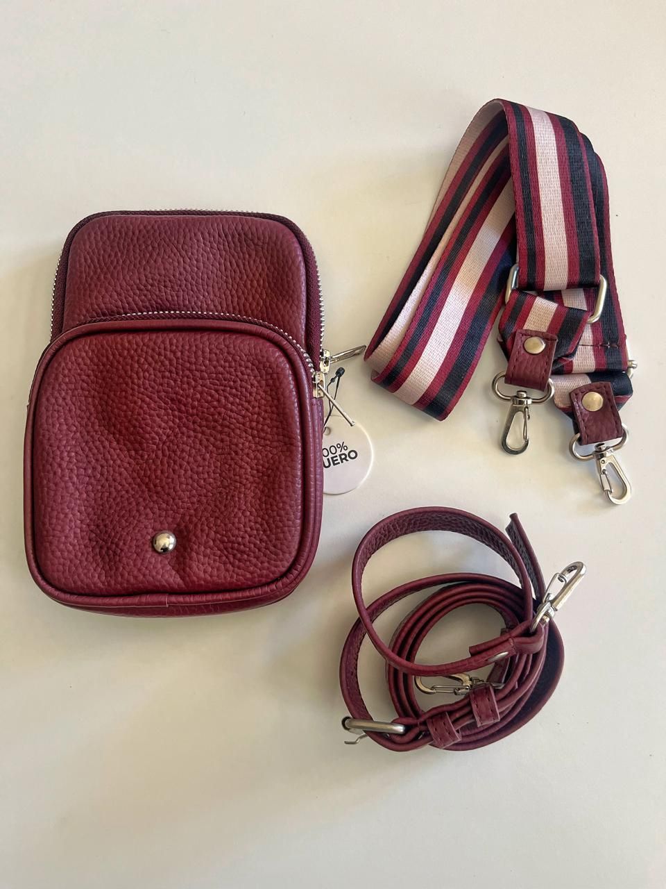 Un bolso bandolera de piel granulada de color burdeos con una correa de rayas estampadas y una correa de piel fina a juego.