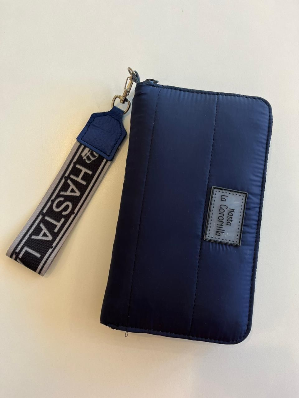 Una billetera rectangular azul marino con cremallera, una correa de muñeca gris