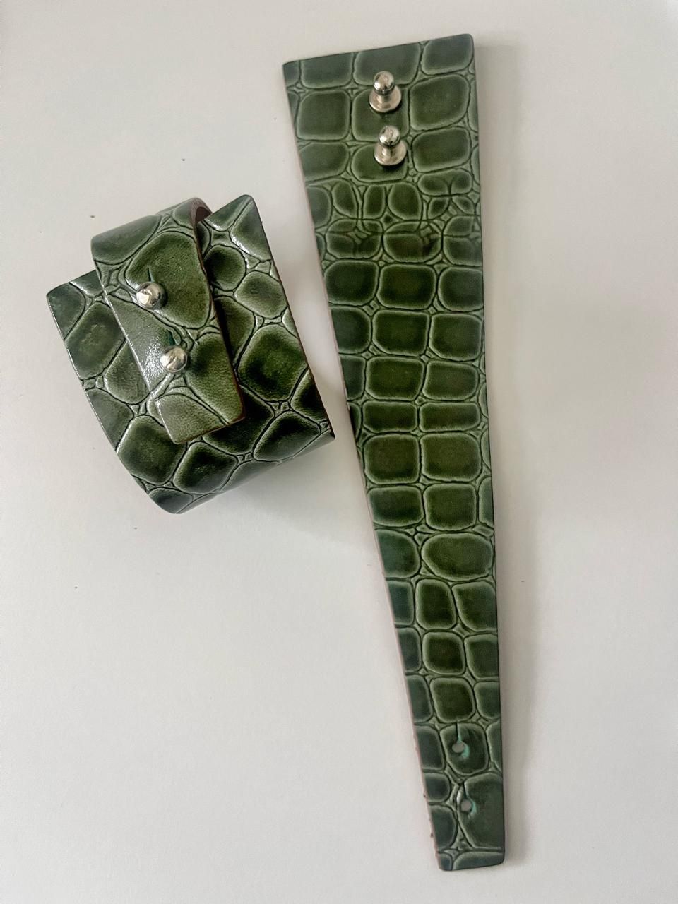Dos puños de piel sintética de cocodrilo de color verde oliva con botones plateados sobre fondo blanco.