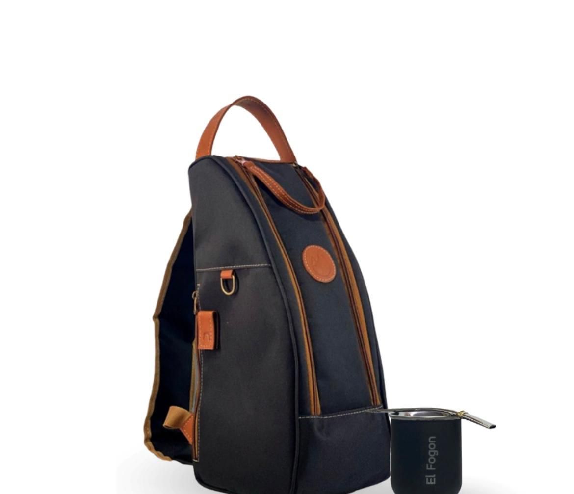 Una mochila negra con detalles de cuero color canela y una taza de marca a juego junto a ella sobre un fondo blanco.