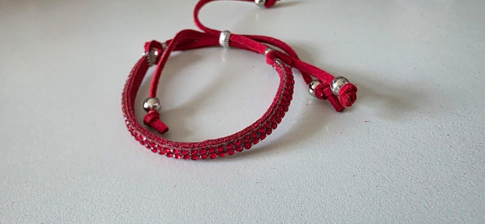 Una pulsera envolvente adornada con cristales rojos y cuentas plateadas sobre una superficie blanca.