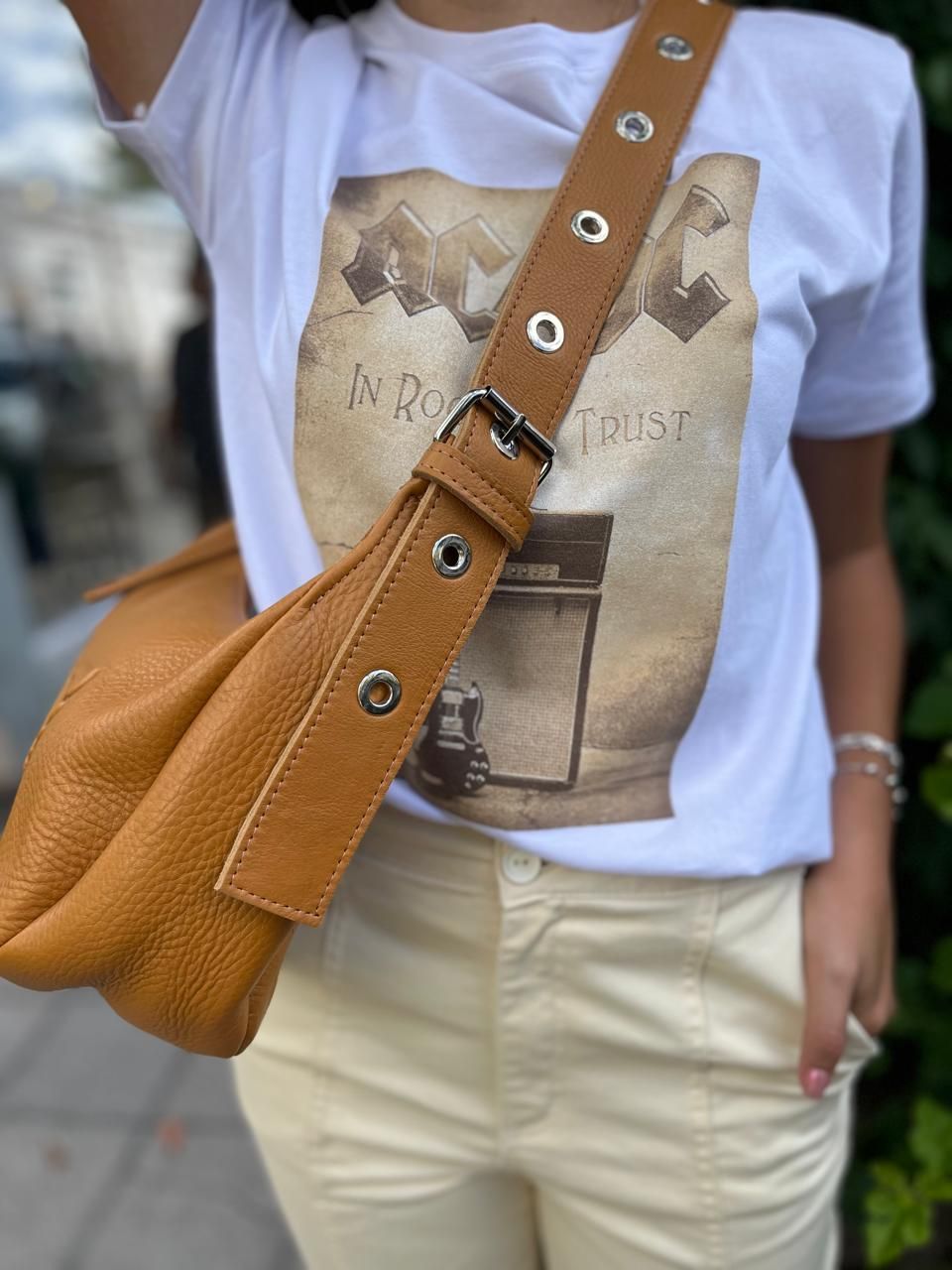 Un bolso estilo hobo de cuero color canela con un logotipo de corazón alado en relieve, que se usa sobre el hombro