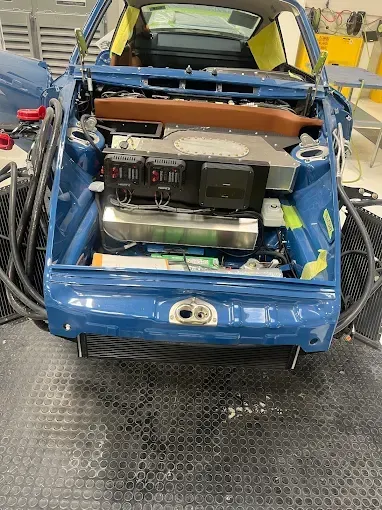 A person in a blue uniform working on a car engine while holding a wrench.