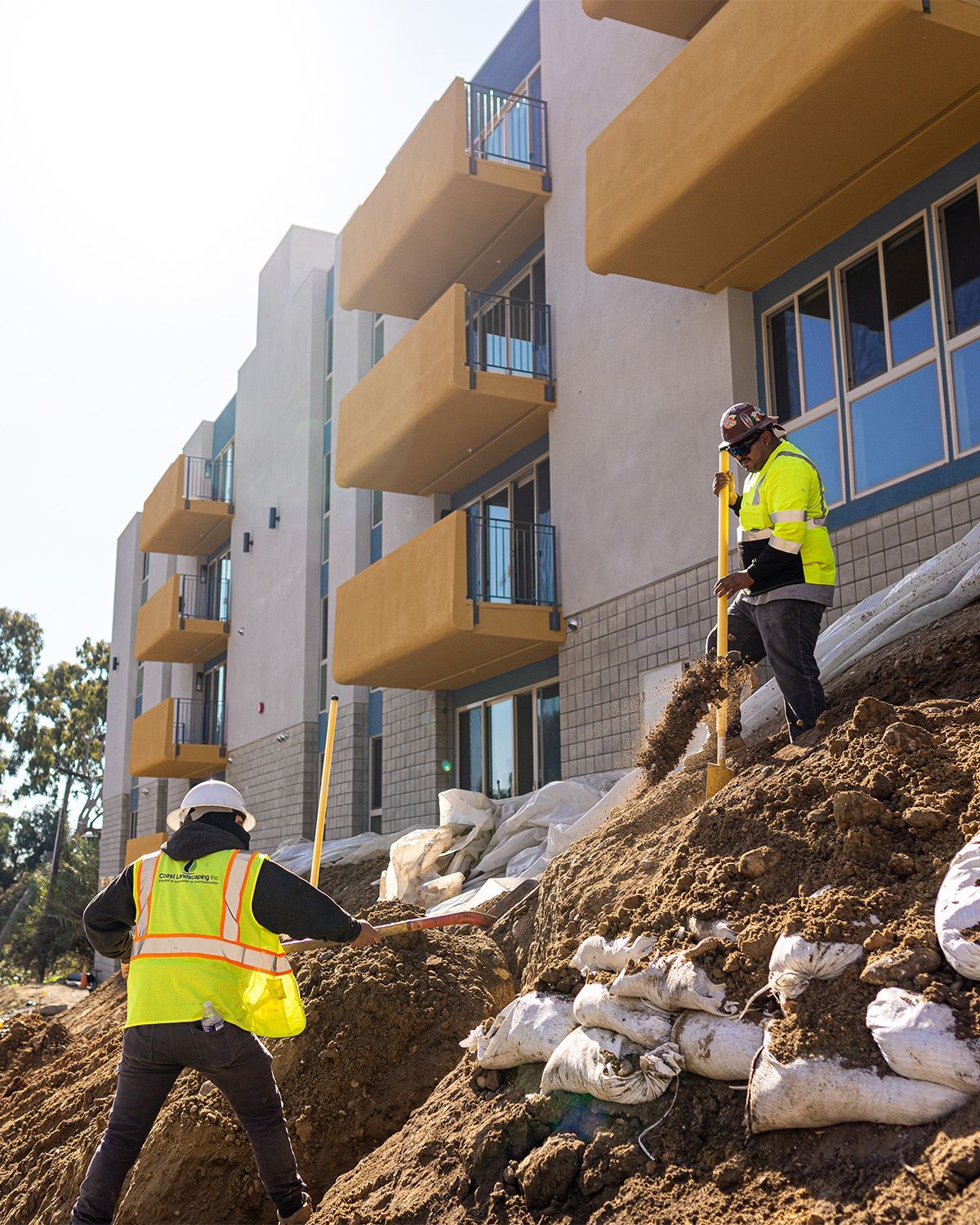 Two construction workers standing on top of a pile of dirt in front of a building