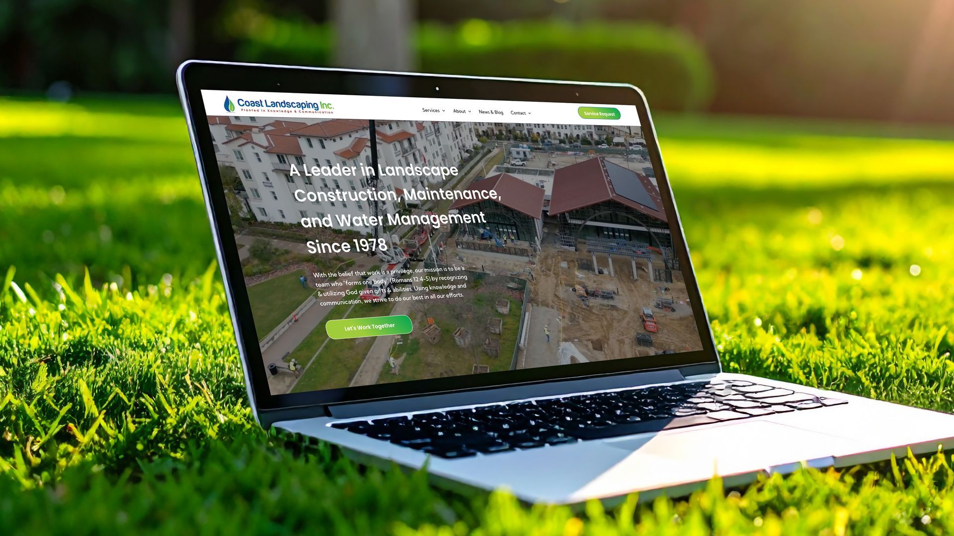Laptop on grass displaying a website. Website features construction in progress, green and white accents.