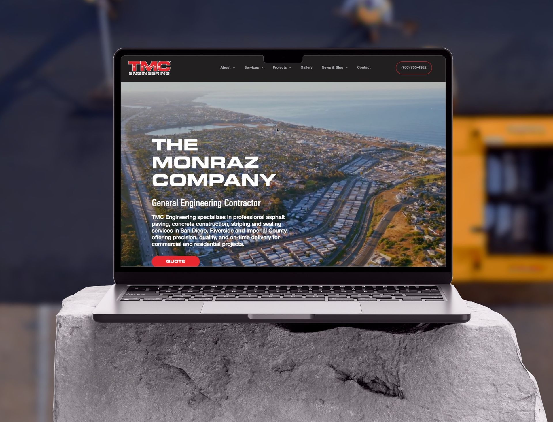 Laptop displaying The Monraz Company website, set against a coastal aerial view.