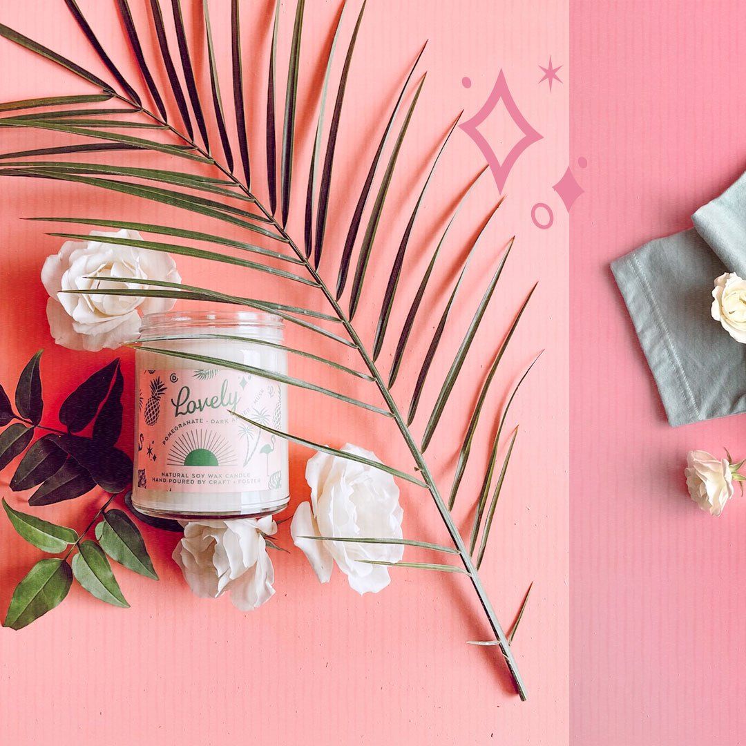 A candle is surrounded by flowers and palm leaves on a pink surface.