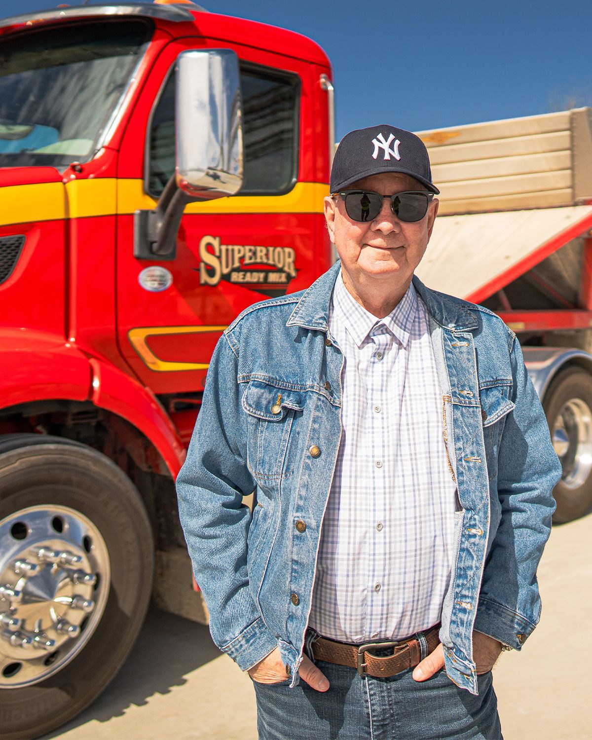 A man wearing a ny hat and sunglasses is standing in front of a red truck.