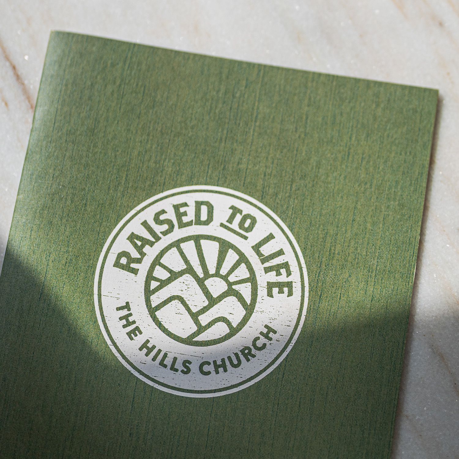 A green paper with a raised to life logo on it