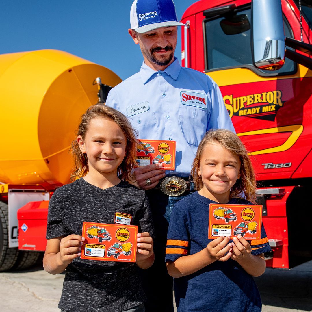 A man and two girls are standing in front of a superior ready mix truck