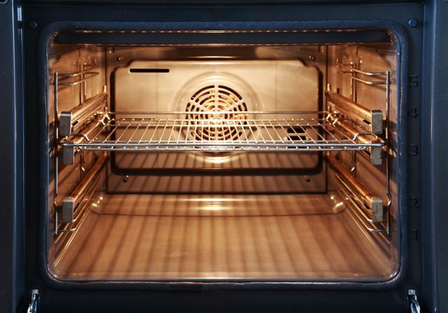 Empty stainless steel oven interior with racks and a lit back fan