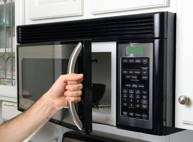 Hand opening a black microwave oven door in a kitchen