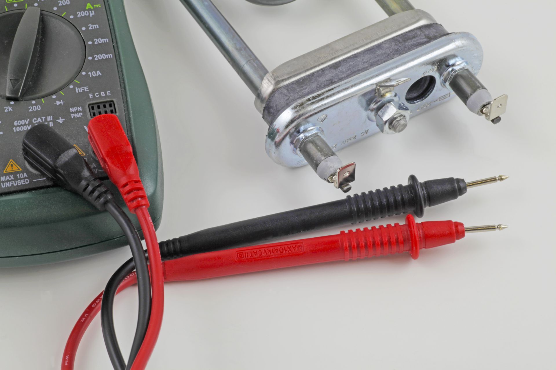 Red and black multimeter probes beside a digital multimeter and a metal electrical component.