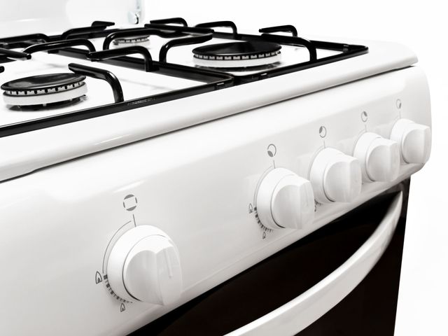 White gas stove with four burners and front control knobs, viewed at an angle