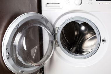 Open front-loading washing machine with door ajar and stainless steel drum visible