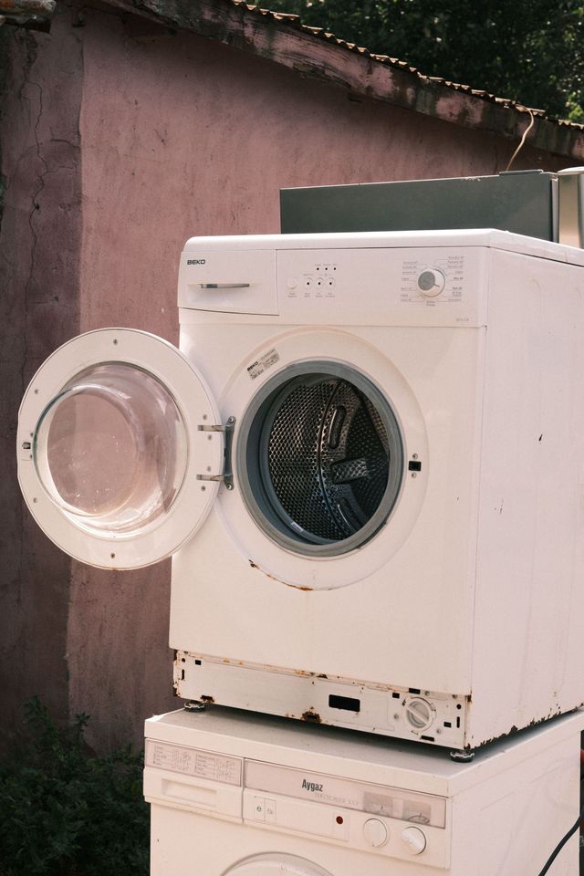 White front-loading washing machine with open door outdoors against a pink wall