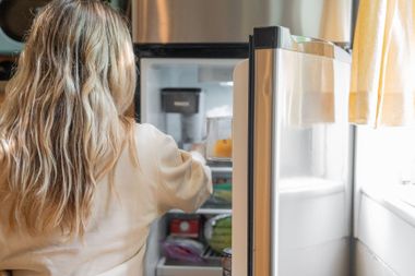 Person opening a refrigerator in a bright kitchen, seen from behind