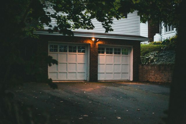 Two-car garage with lit porch light under trees at dusk