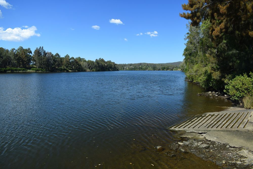 Calm Lake Under a Blue Sky, with Trees Lining the Shore — Mid Coast Tile Co in Tinonee, NSW