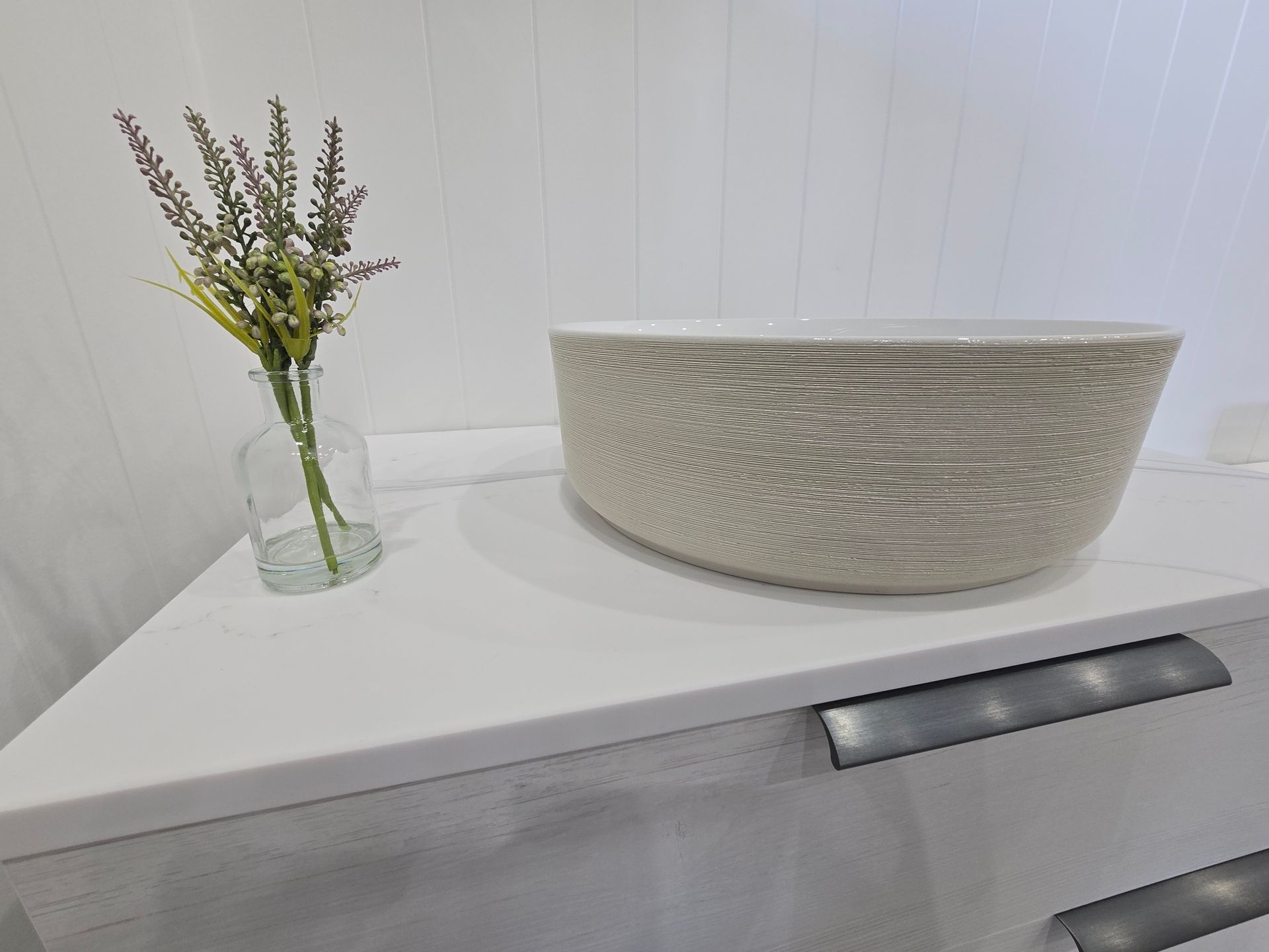 A White Bathroom Sink with A Beige Bowl, a Small Vase of Flowers — Mid Coast Tile Co in Taree, NSW