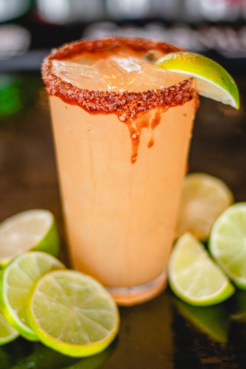 A close up of a drink in a glass with limes on a table.