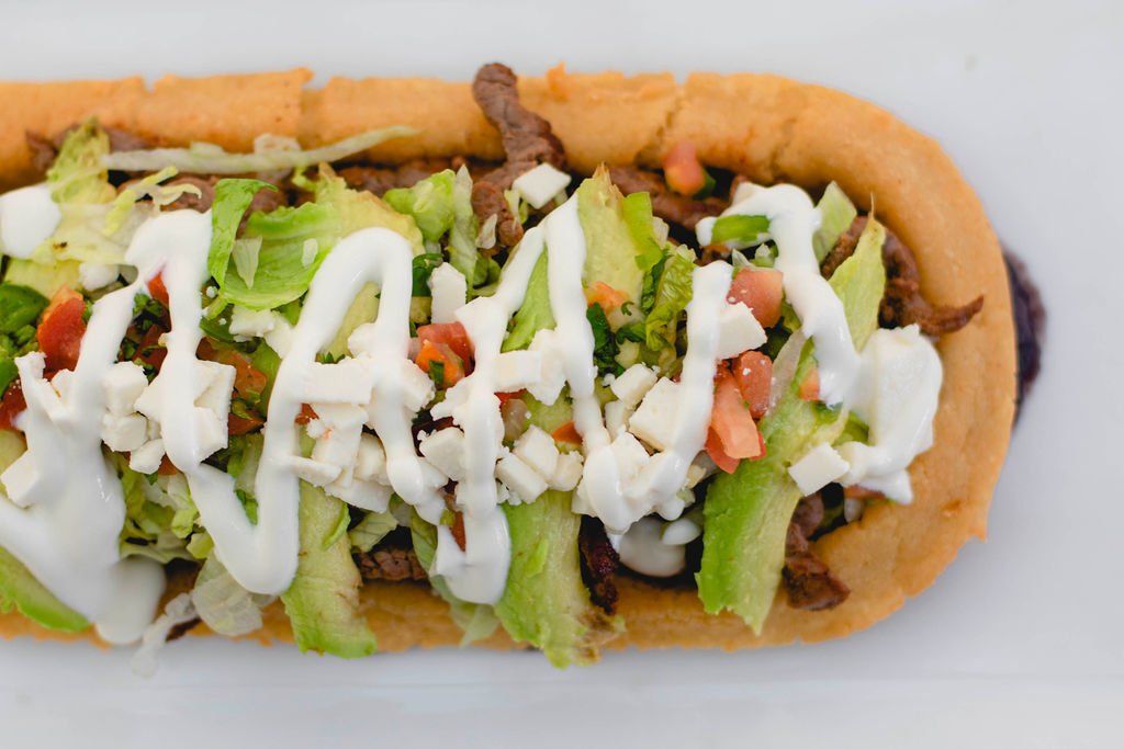 A sub sandwich with lettuce , tomatoes , and sour cream on a white plate.