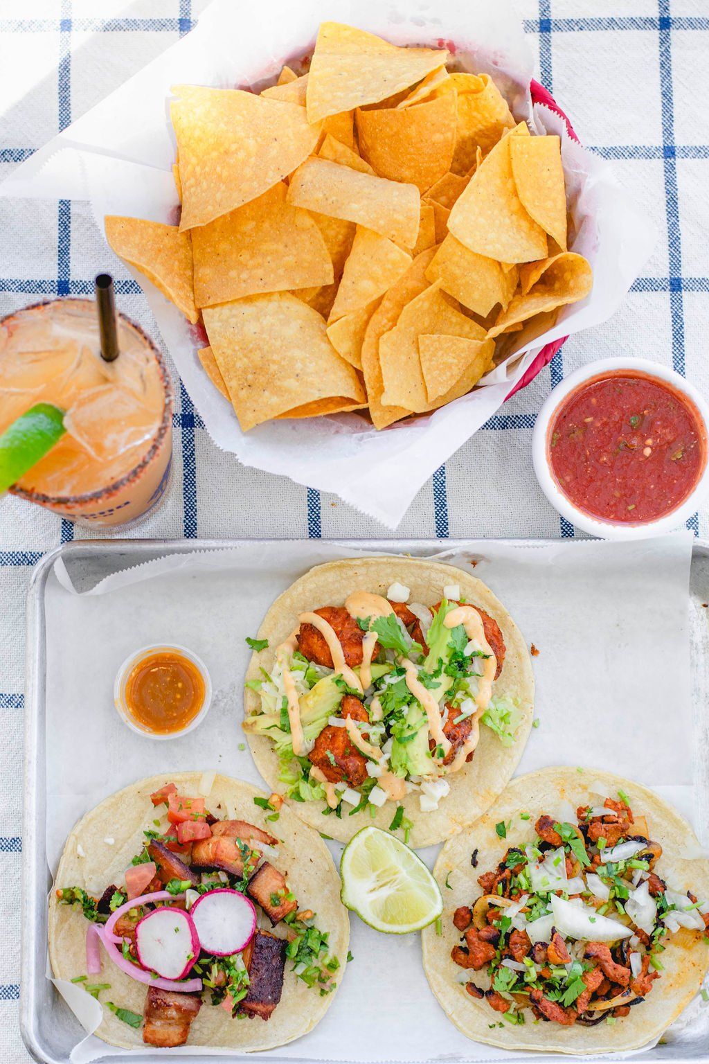 A tray of tacos , chips , salsa and a drink on a table.