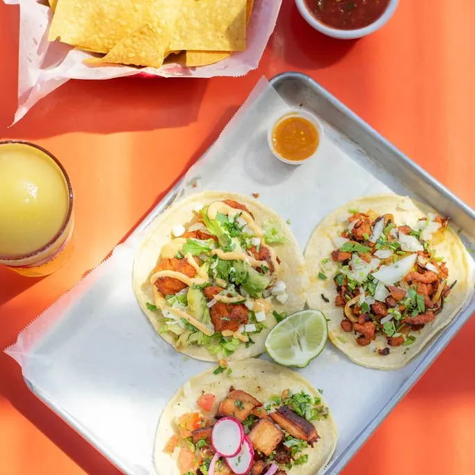 A tray of tacos sits on a table next to a bowl of salsa
