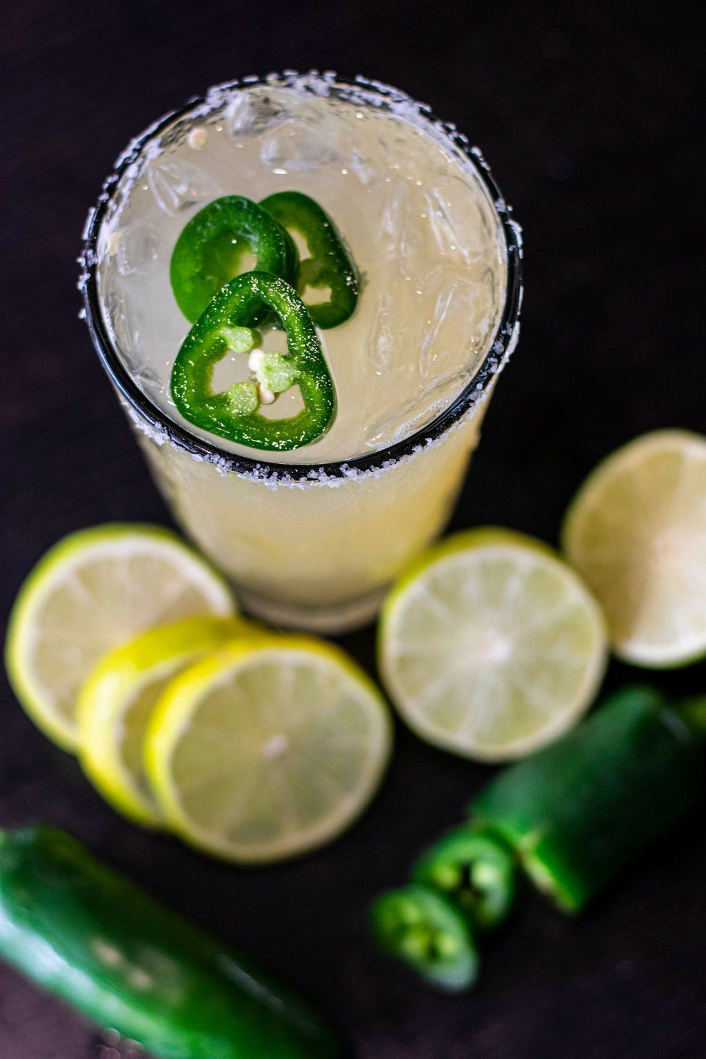 A close up of a margarita with jalapenos and lemon slices