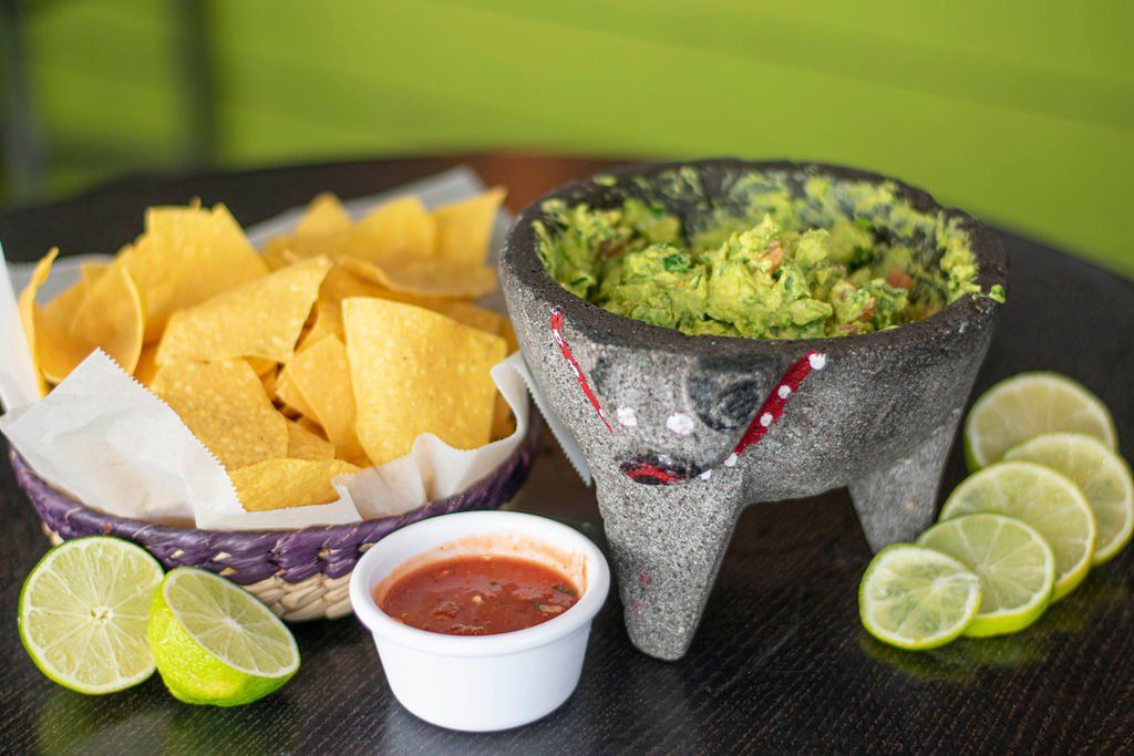 A bowl of guacamole next to a bowl of tortilla chips on a table.