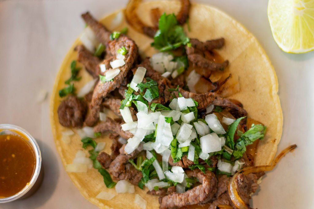 A close up of a taco with meat and onions on a plate.