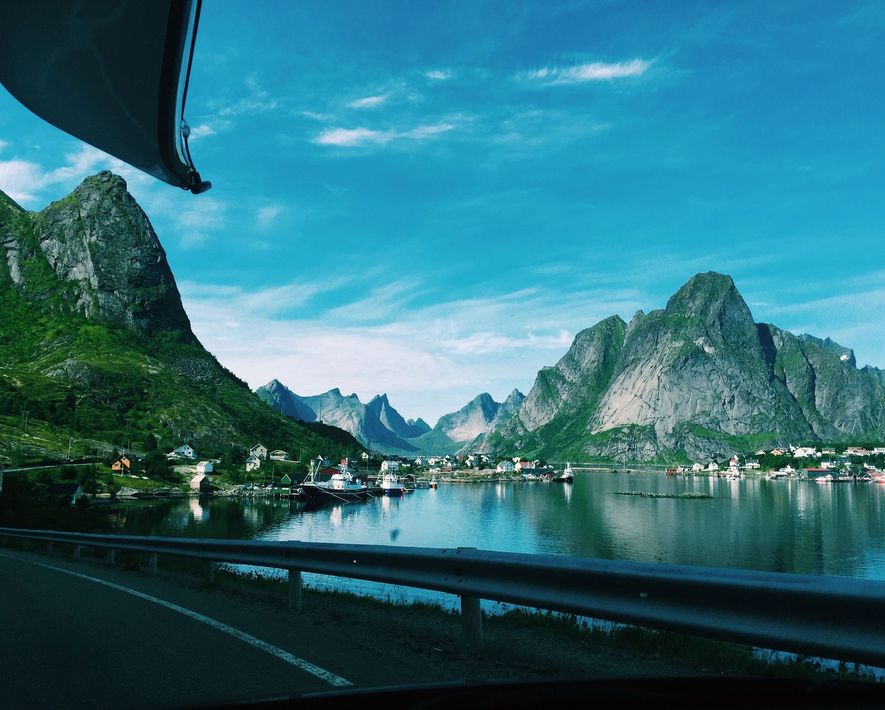Scenic fjord with mountains, calm water, and a coastal road under a bright blue sky