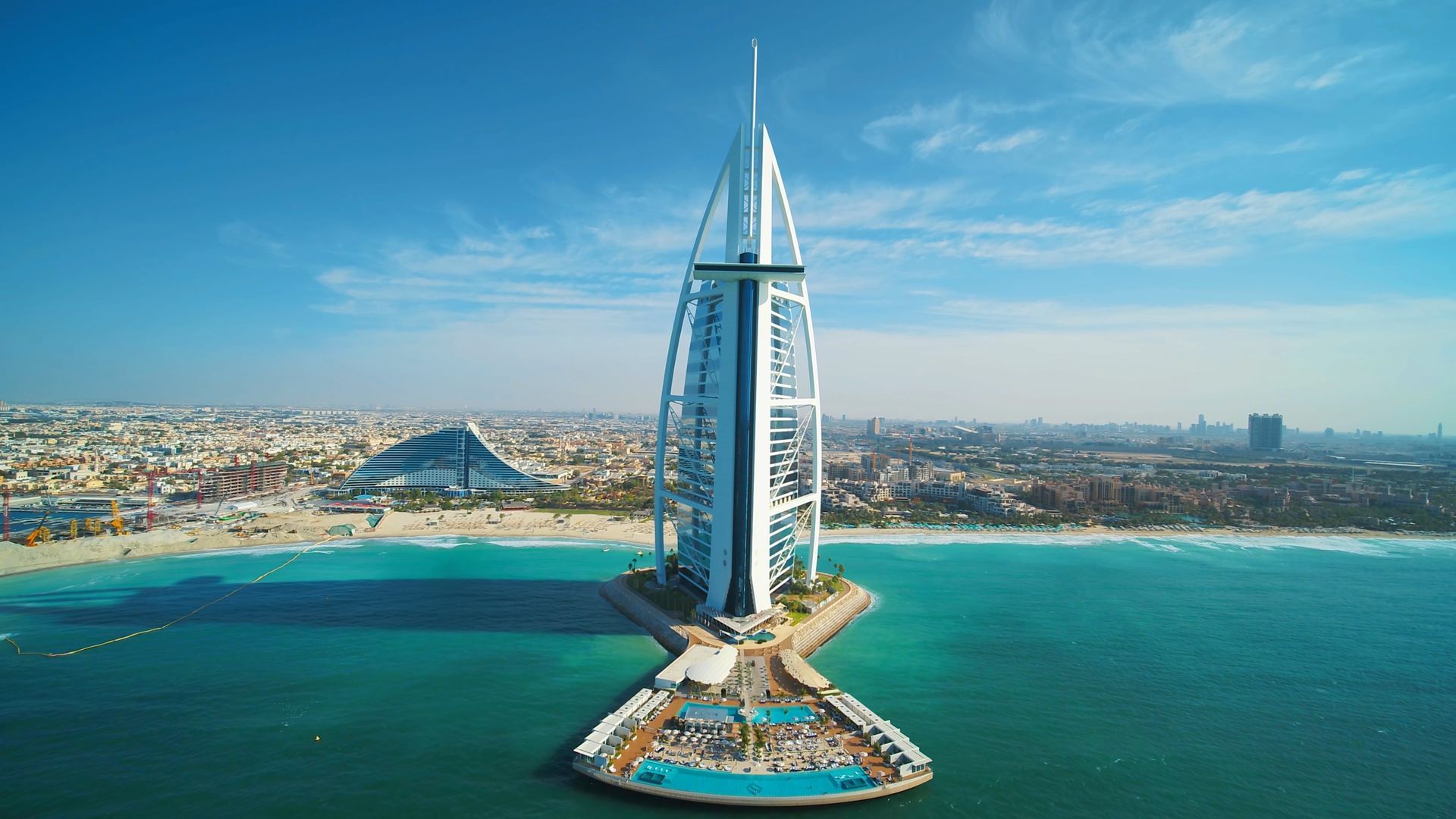Burj Al Arab hotel on a turquoise sea with Dubai skyline and sandy coast in the background