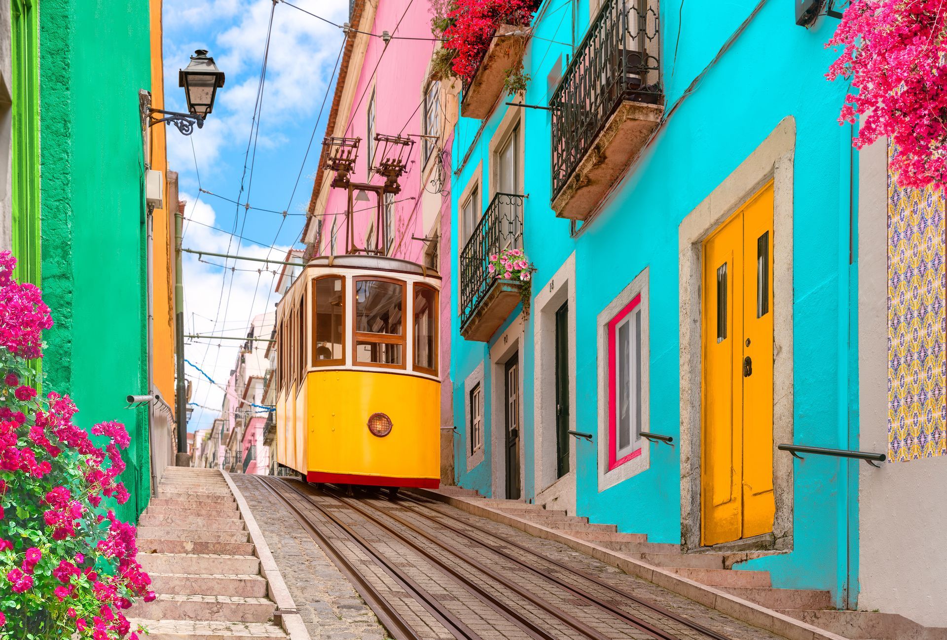 Yellow tram on steep track between bright turquoise and pink buildings in a narrow street