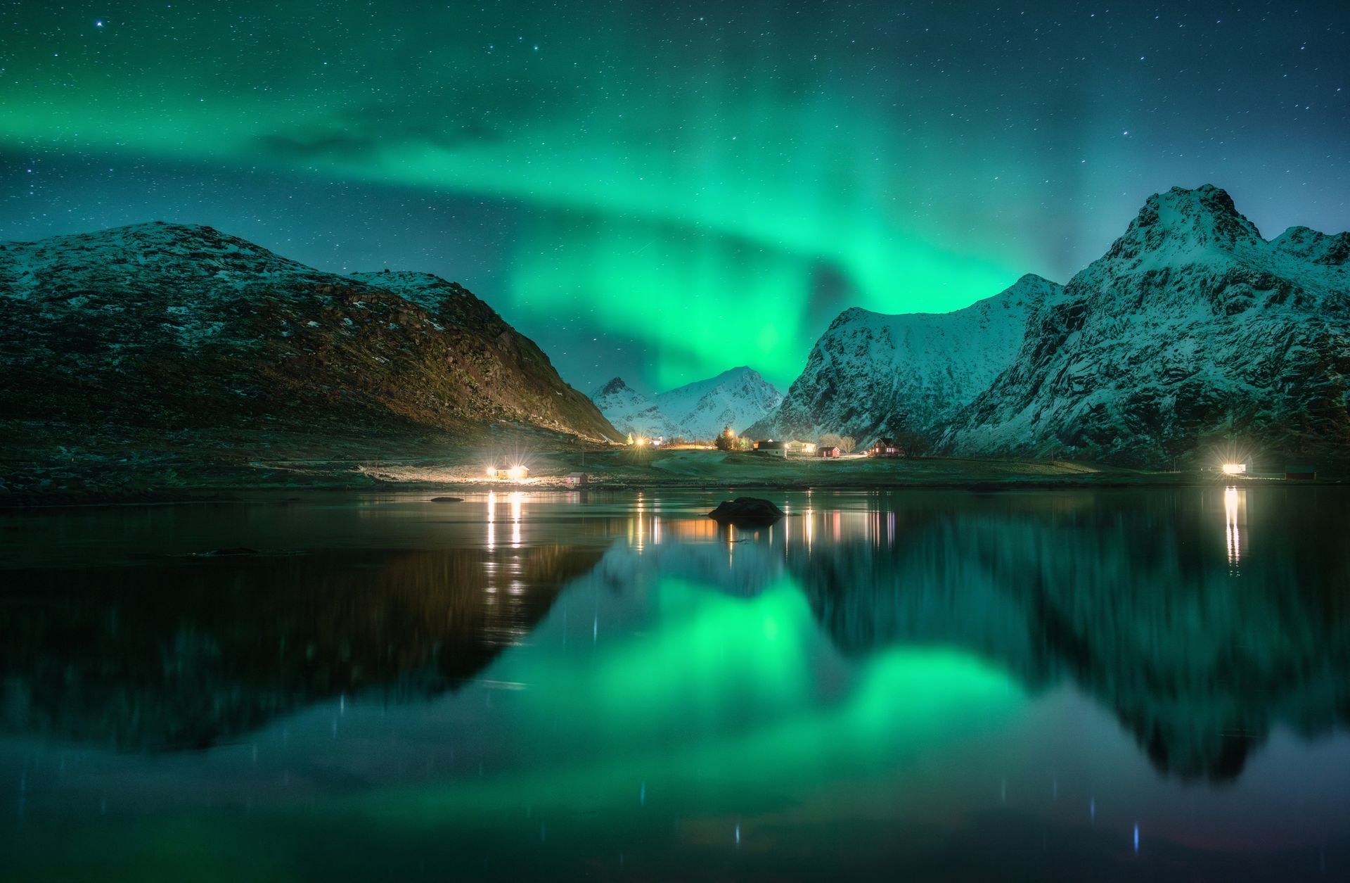 Aurora lights over snowy mountains reflected in a calm dark fjord at night