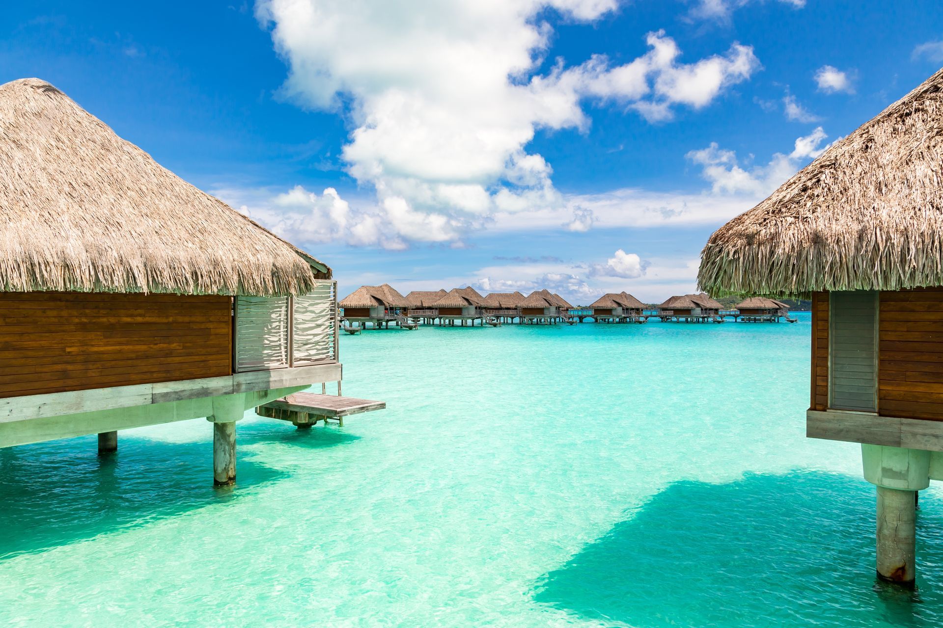Tropical overwater bungalows beside clear turquoise lagoon under a bright blue sky