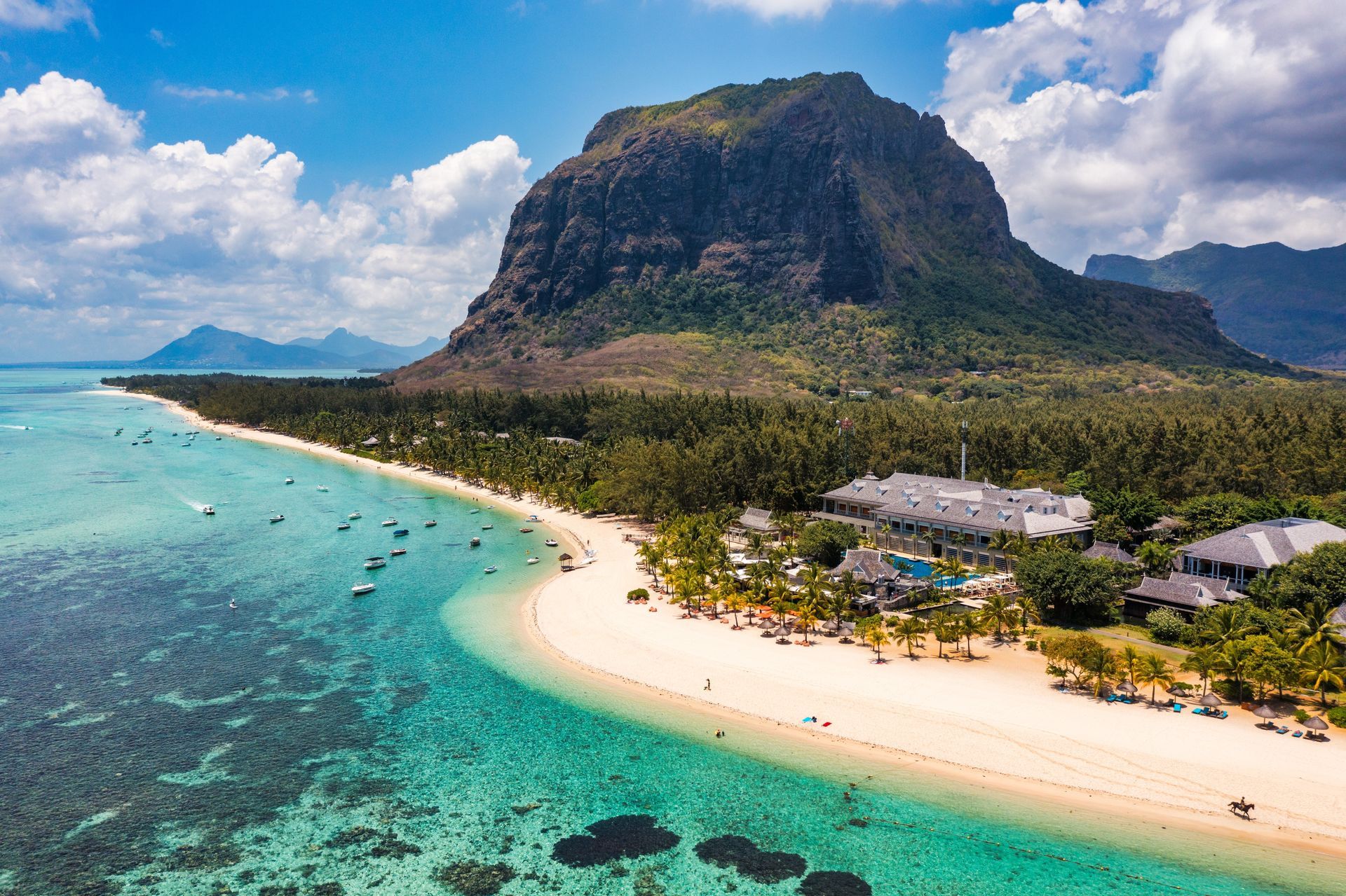 Turquoise lagoon and white sand beach beside a lush green mountain under a bright blue sky