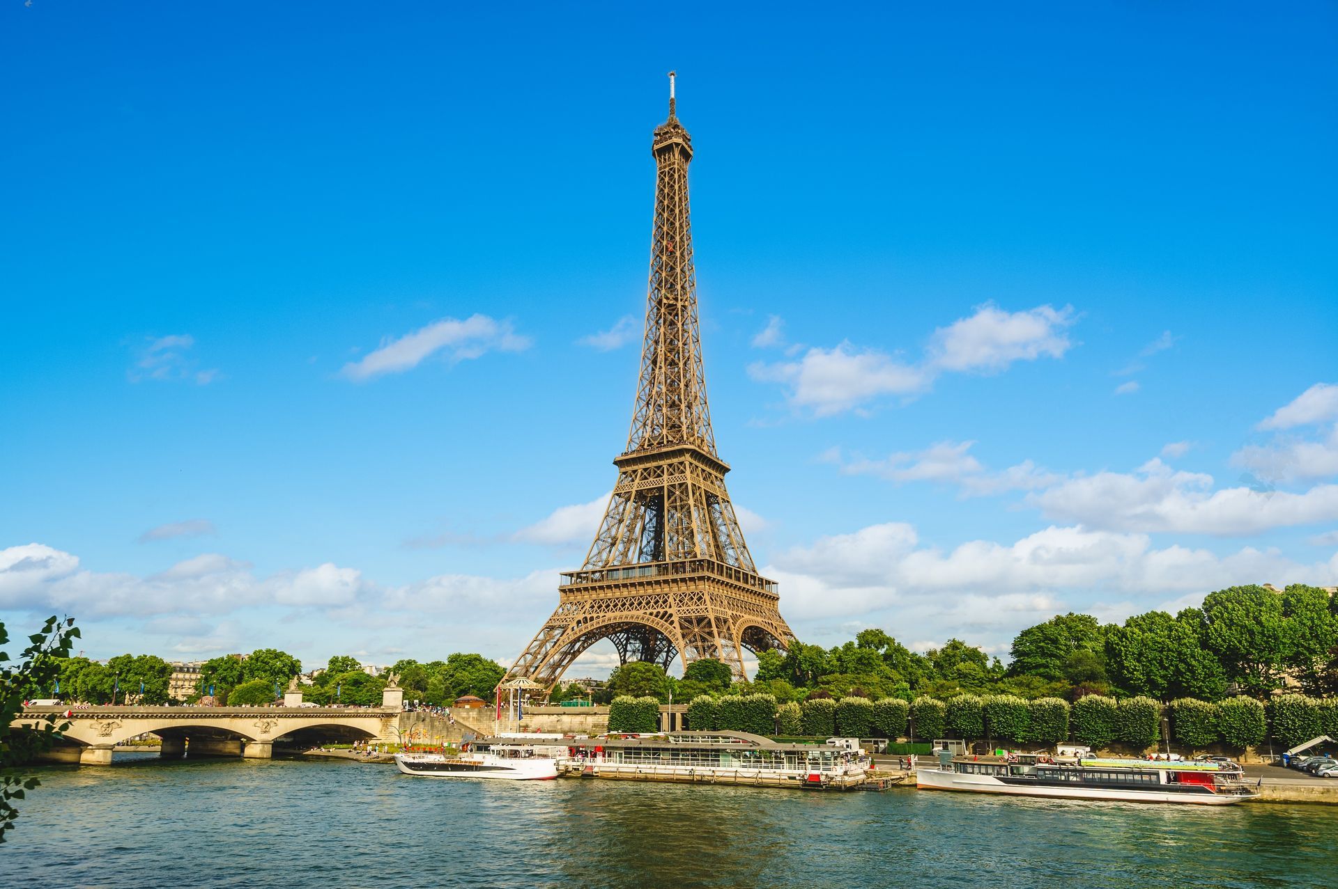 Eiffel Tower above the Seine River on a sunny day with blue sky and green trees