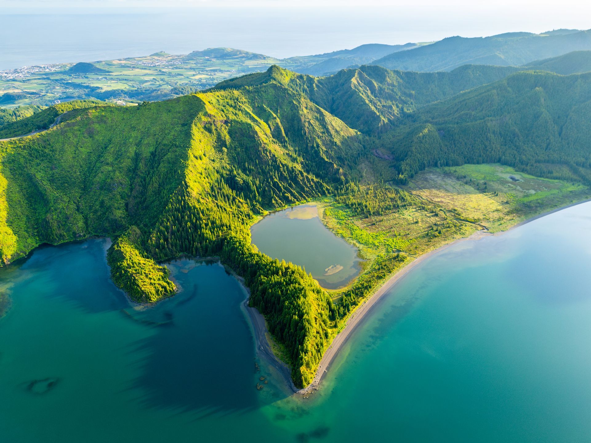 Aerial view of a lush green volcanic peninsula with a lagoon and turquoise ocean on both sides