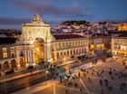 Dusk view of a lit plaza and ornate archway in a historic city square with people walking below