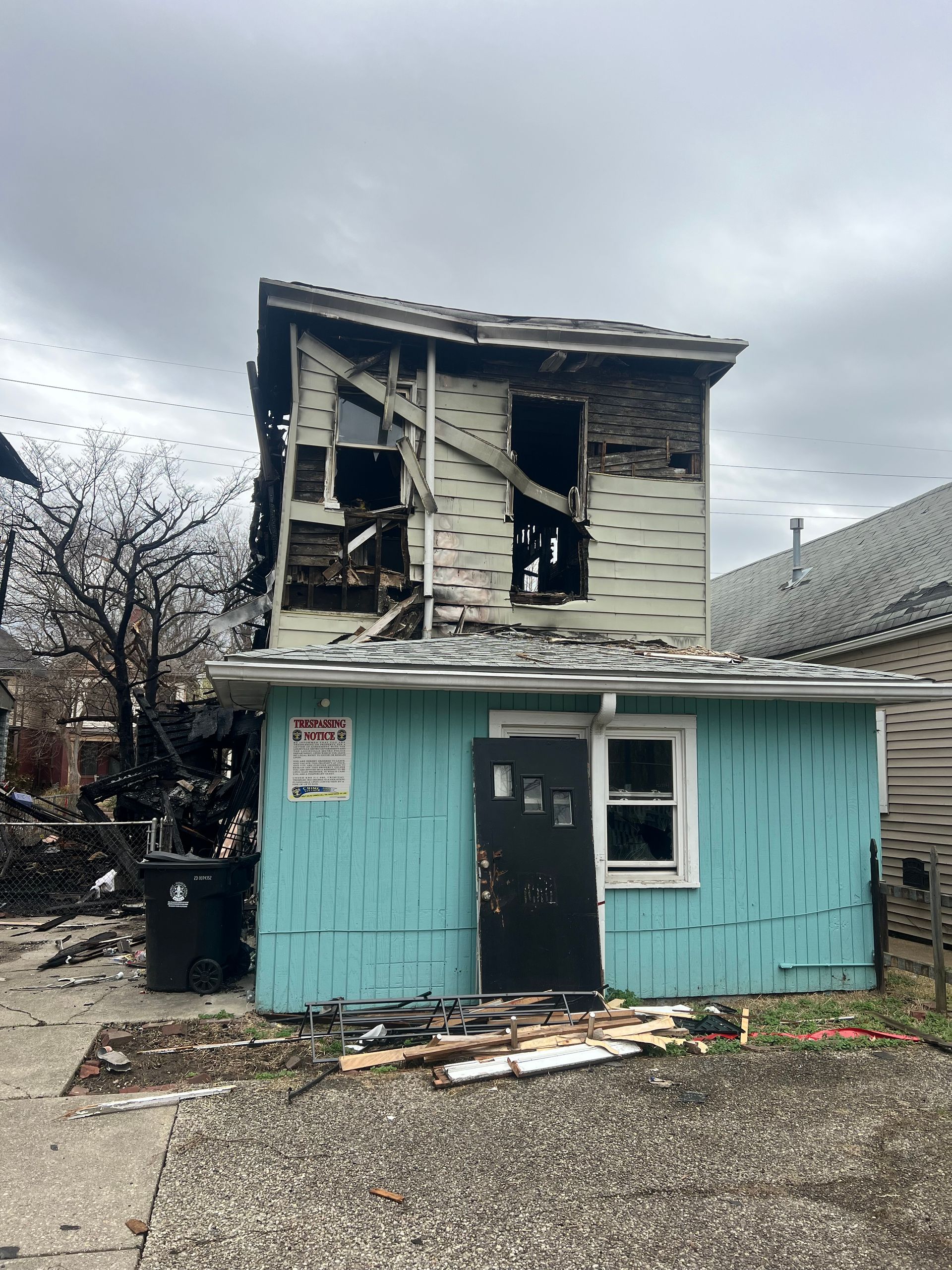 A two-story building with a light blue lower level and fire-damaged upper level with exposed siding and framing.