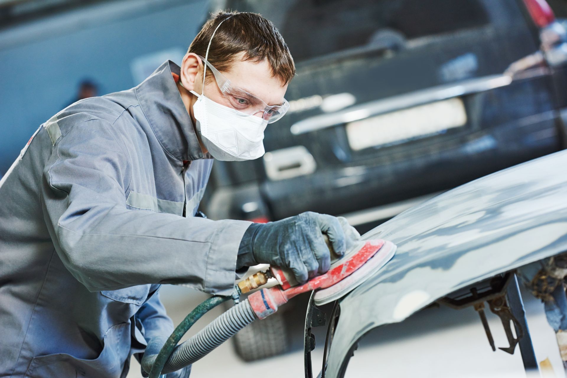 Auto body technician sanding vehicle panel during collision repair preparation