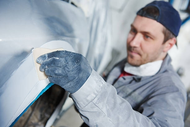 Auto repairman plastering autobody bonnet during collision repair with precision and care.
