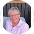 An older woman wearing glasses and a pink shirt is sitting in a chair.