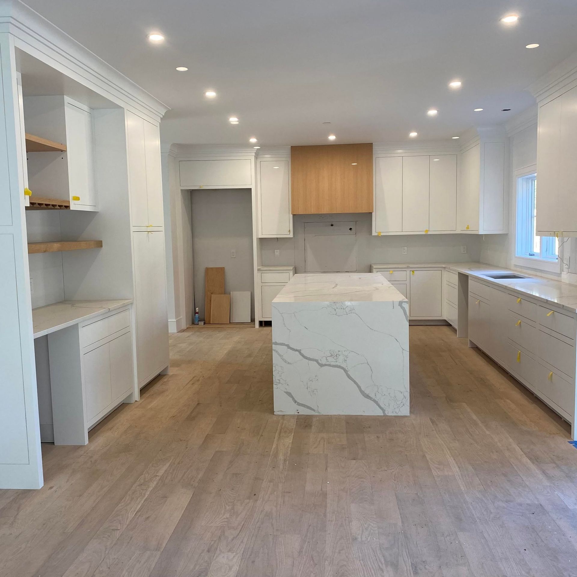 Bright modern kitchen with white cabinets, wood floors, and a marble island.