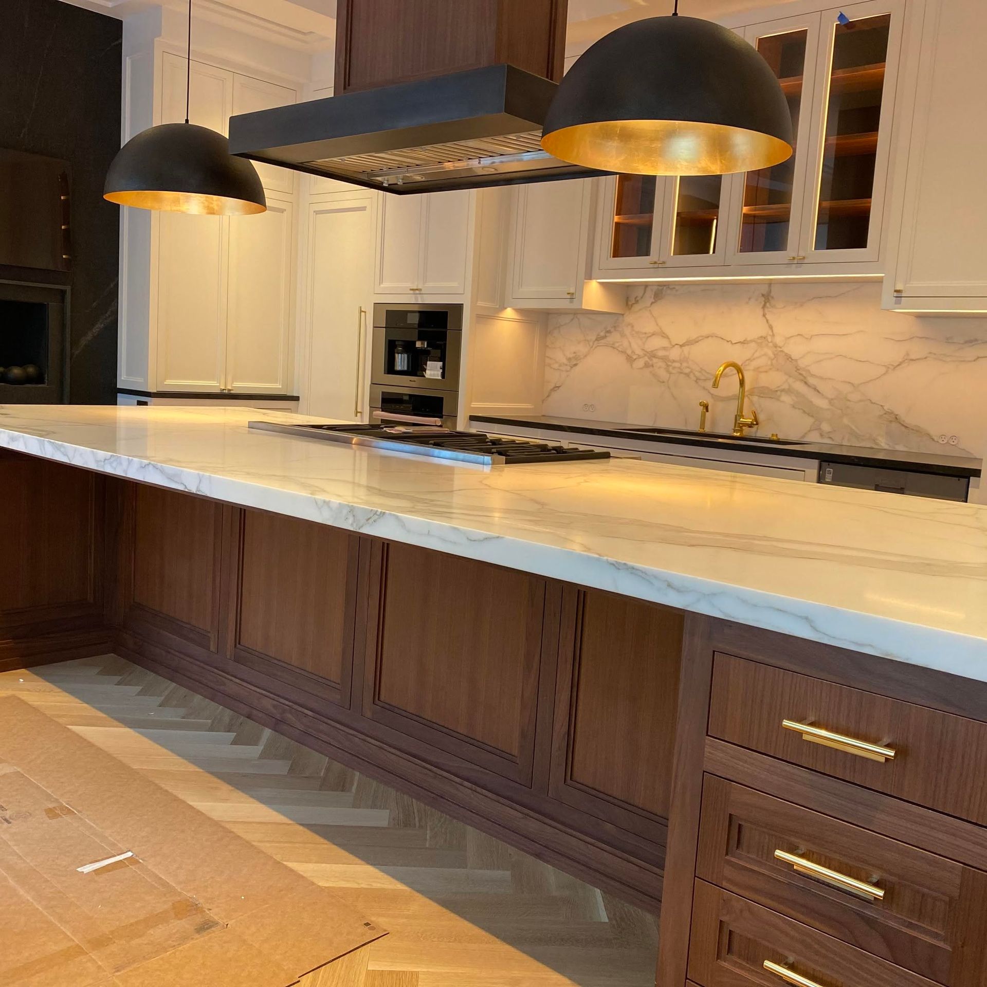Modern kitchen with white cabinets, marble island, dark wood accents, and two black pendant lights