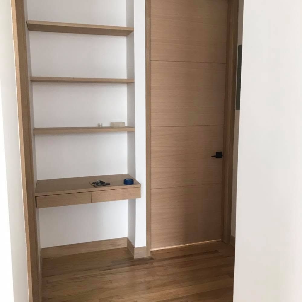 Built-in wooden shelving and a small desk beside a closed wooden door in a minimalist room